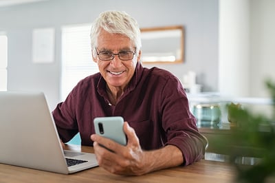mature-man-using-smartphone-front-laptop-computer
