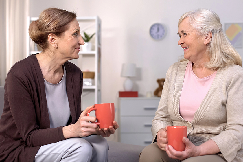 Aged female friends drinking tea and chatting sitting in comfortable living room