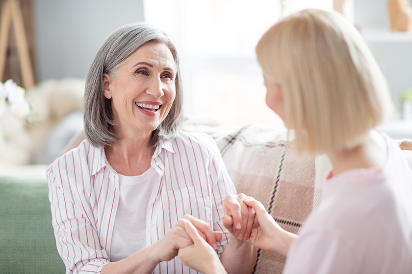 Photo of pretty positive ladies sit on couch hold hands look each other have good mood spend free time indoors